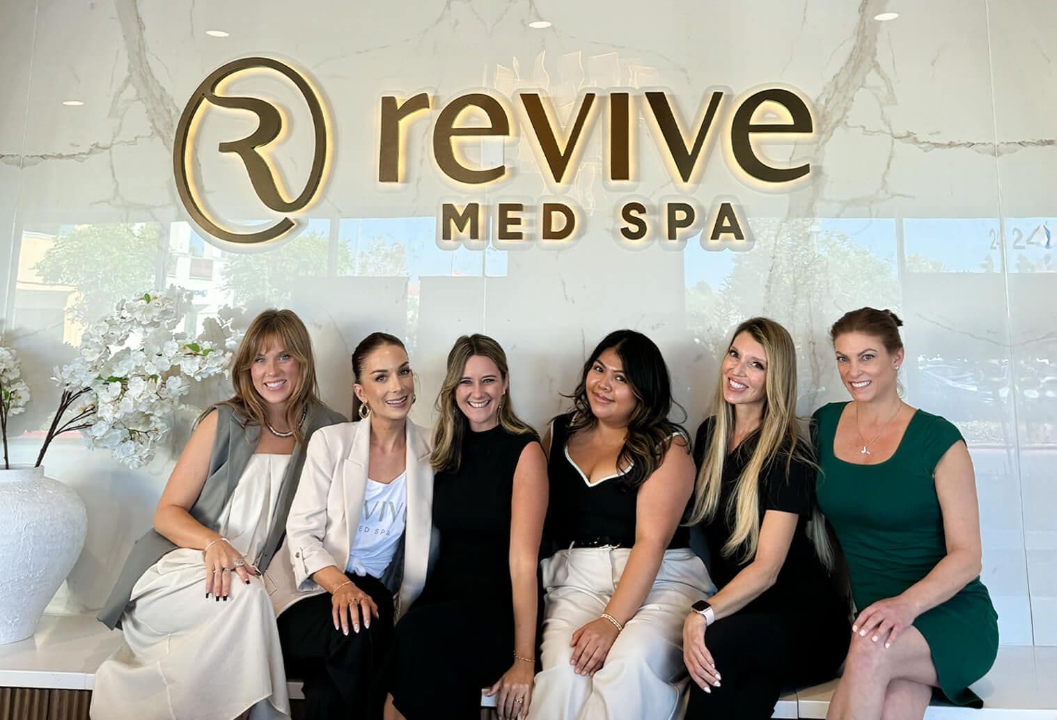 Six women sitting in front of a Revive Med Spa sign