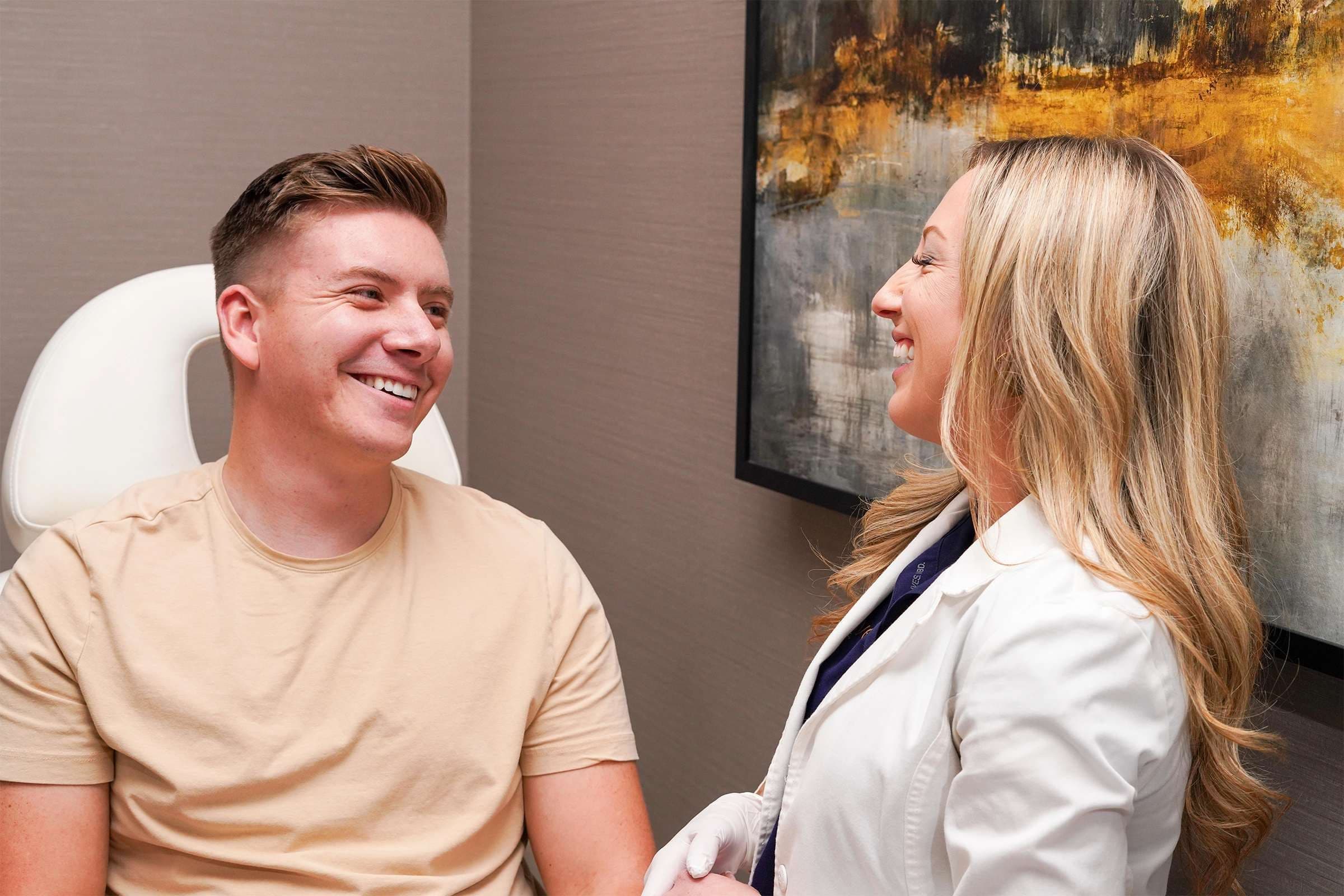 Female medical provider in white jacket speaking to a male client in a tan shirt. Both are smiling.