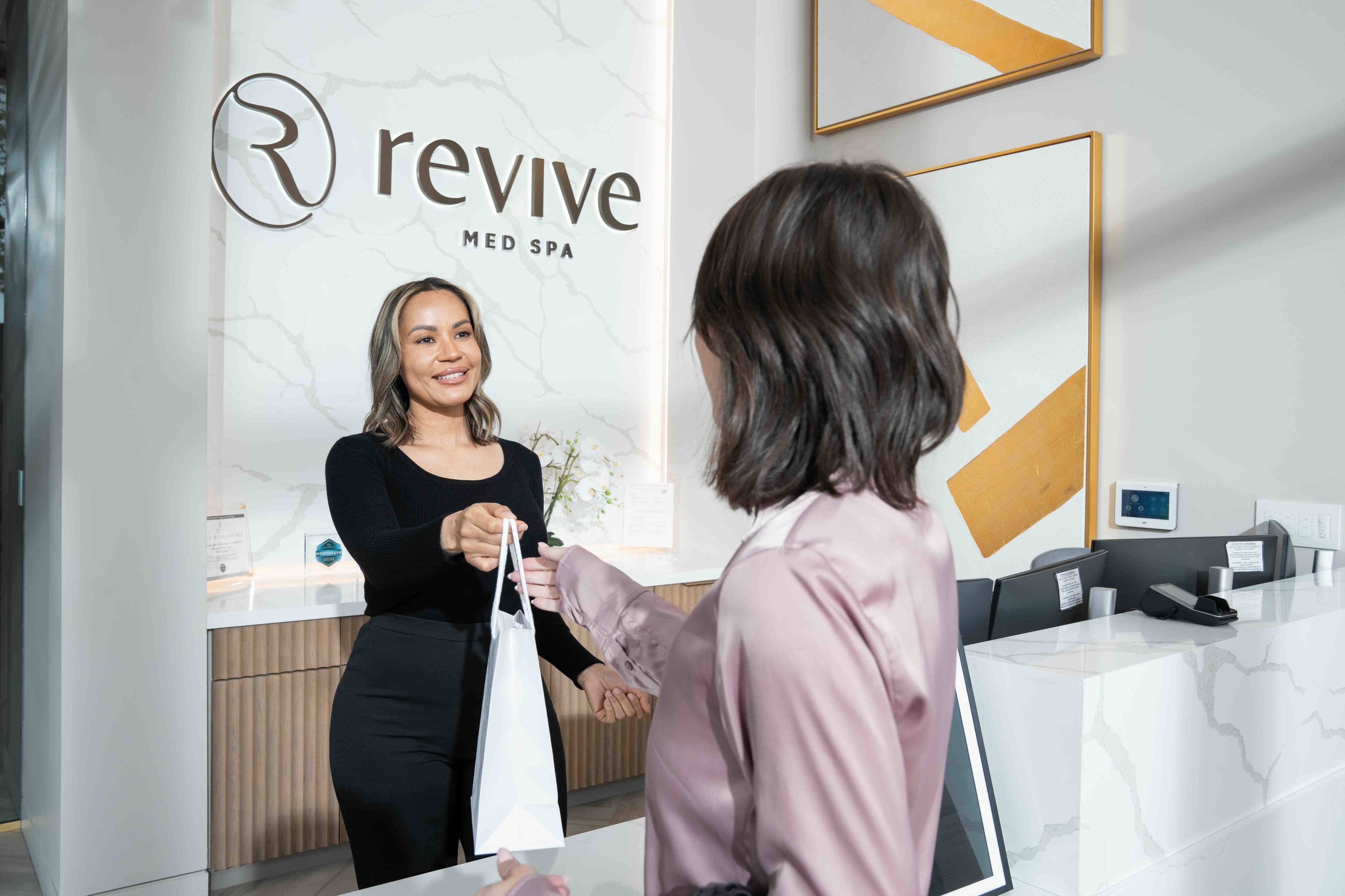 Smiling Woman Handing Gift Bag Across the counter to Another Woman